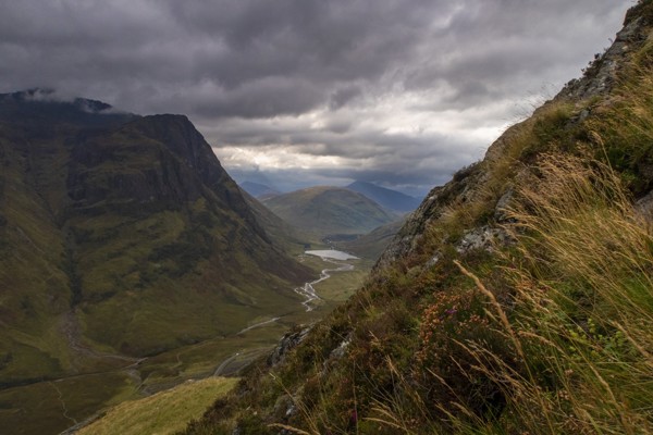 Dramatic view of the Glencoe valley in the Scottish Highlands, with dark, cloudy skies and sunlight breaking through over the mountains in the distance. ?? ''