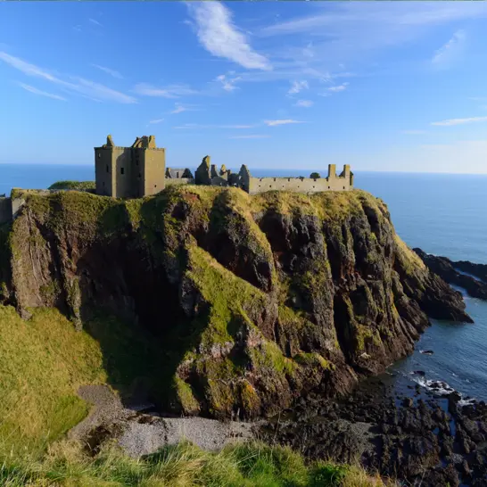 Dunnottar Castle ruins perched dramatically on a sea cliff overlooking the North Sea under a bright blue sky near Stonehaven, Scotland. ?? ''